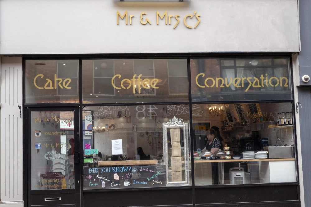 The outside of the cafe, with the slogan 'Cake, Coffee, Conversation' in gold writing in the windows.