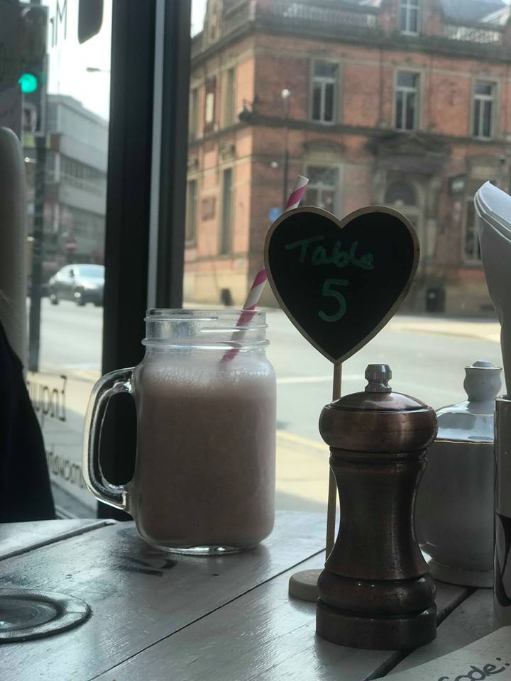 The table number written on a small chalkboard style love heart, with Wakefield captured behind outside the window. A strawberry smoothie in a mason jar glass is too photographed. 
